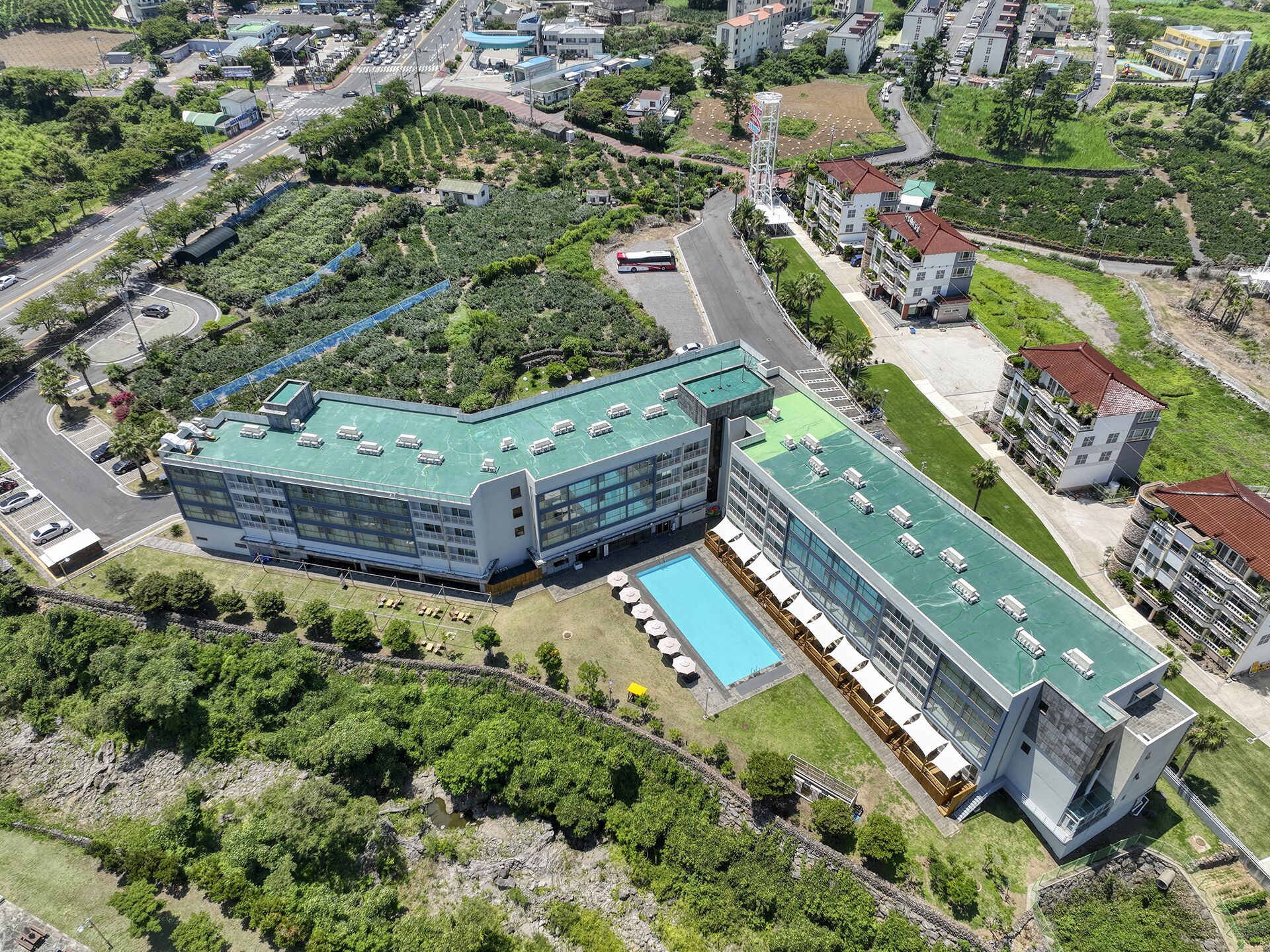 Un hôtel moderne doté d’une piscine sur le toit, entouré d’une végétation luxuriante et situé à proximité d’une route.