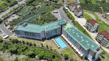 Un hôtel moderne doté d’une piscine sur le toit, entouré d’une végétation luxuriante et situé à proximité d’une route.