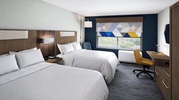 A hotel room with two beds, a desk, a chair, and a window with a view.