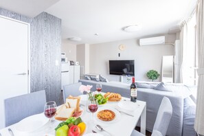A dining area with a table set for two, a television in the background, and a living area with a sofa and a plant.