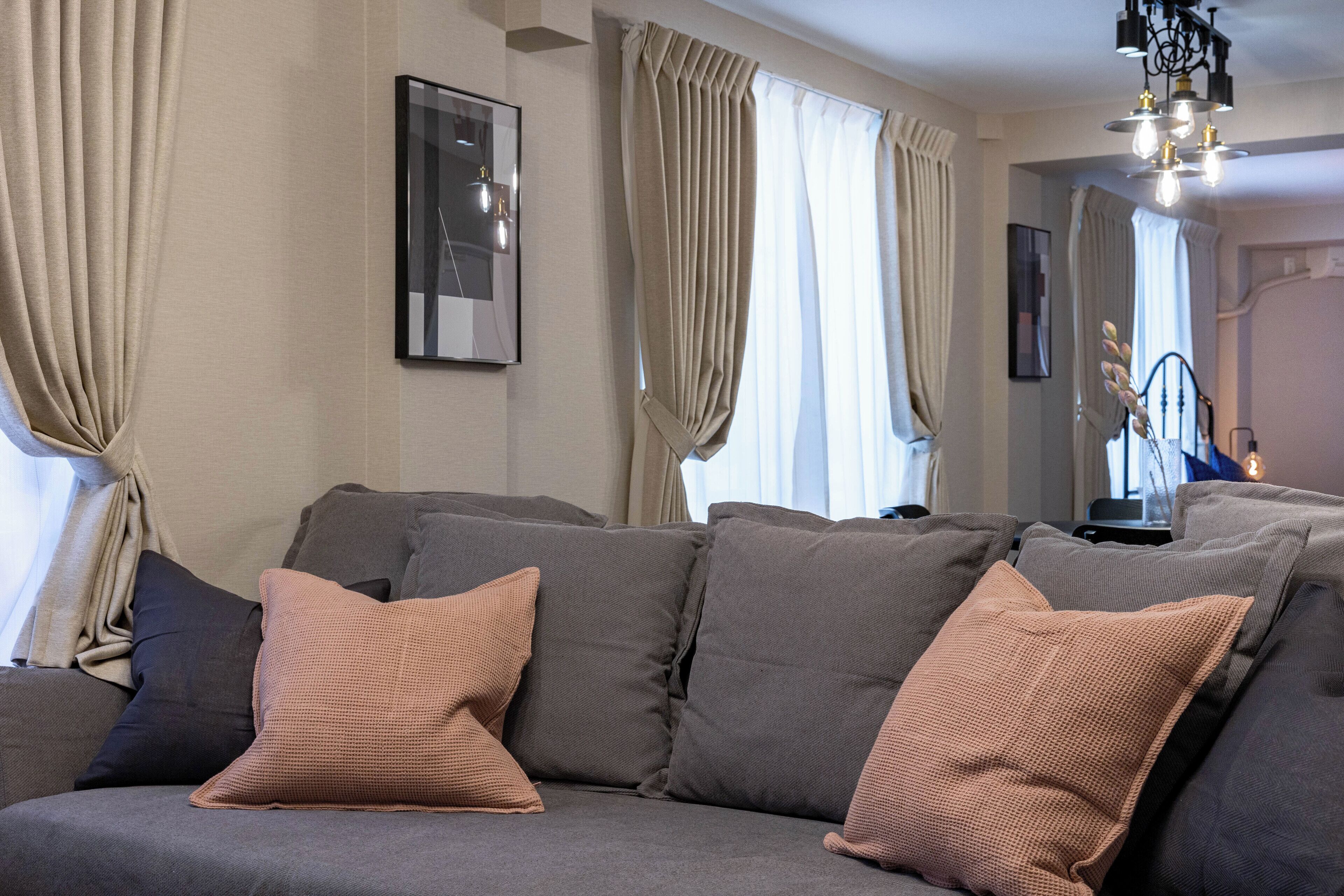 A modern living room with a grey sectional sofa, beige curtains, and a chandelier.