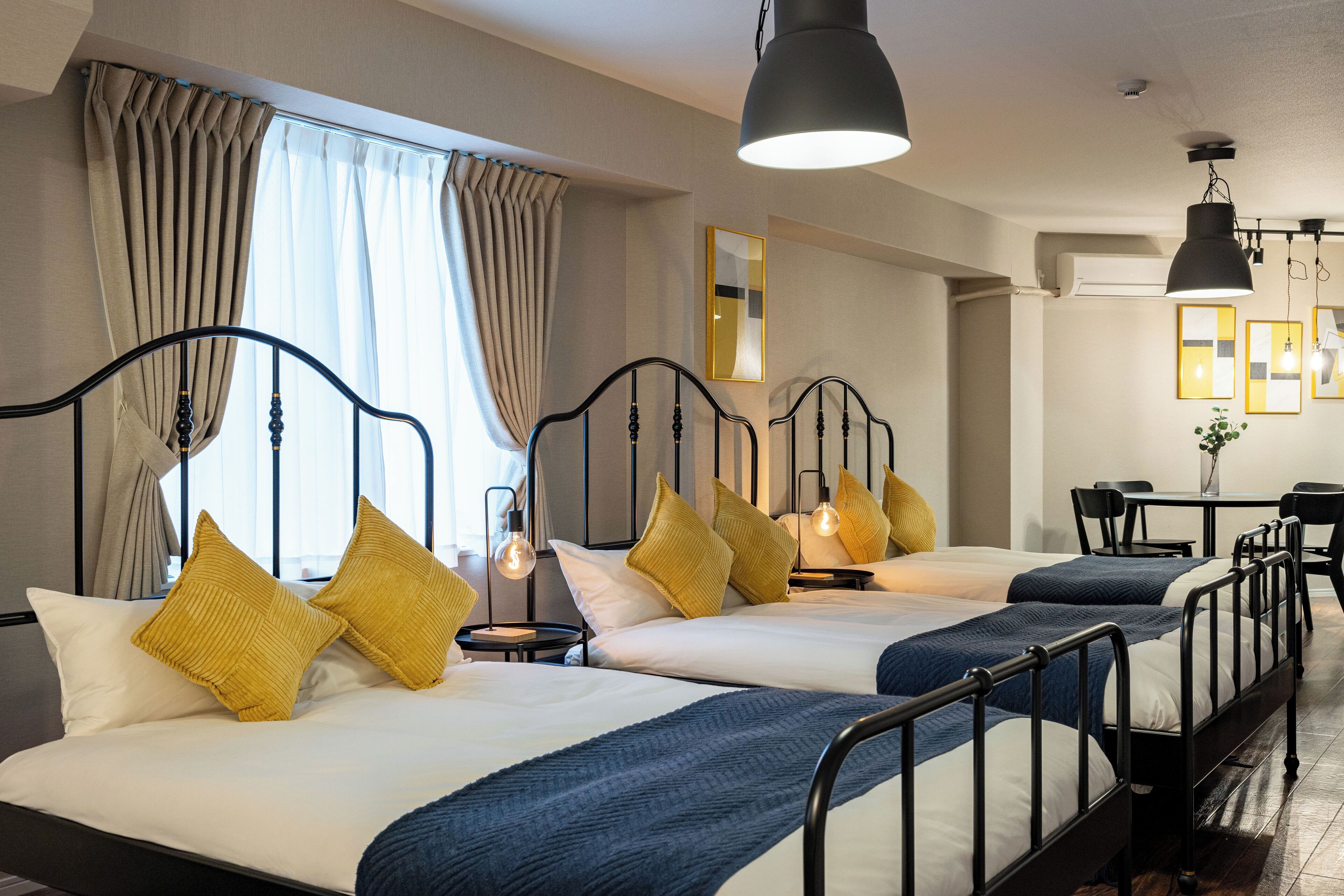 Une chambre d’hôtel avec trois lits, chacun doté d’une tête de lit, de tables de chevet et de lampes. La chambre comprend également un bureau et une chaise.