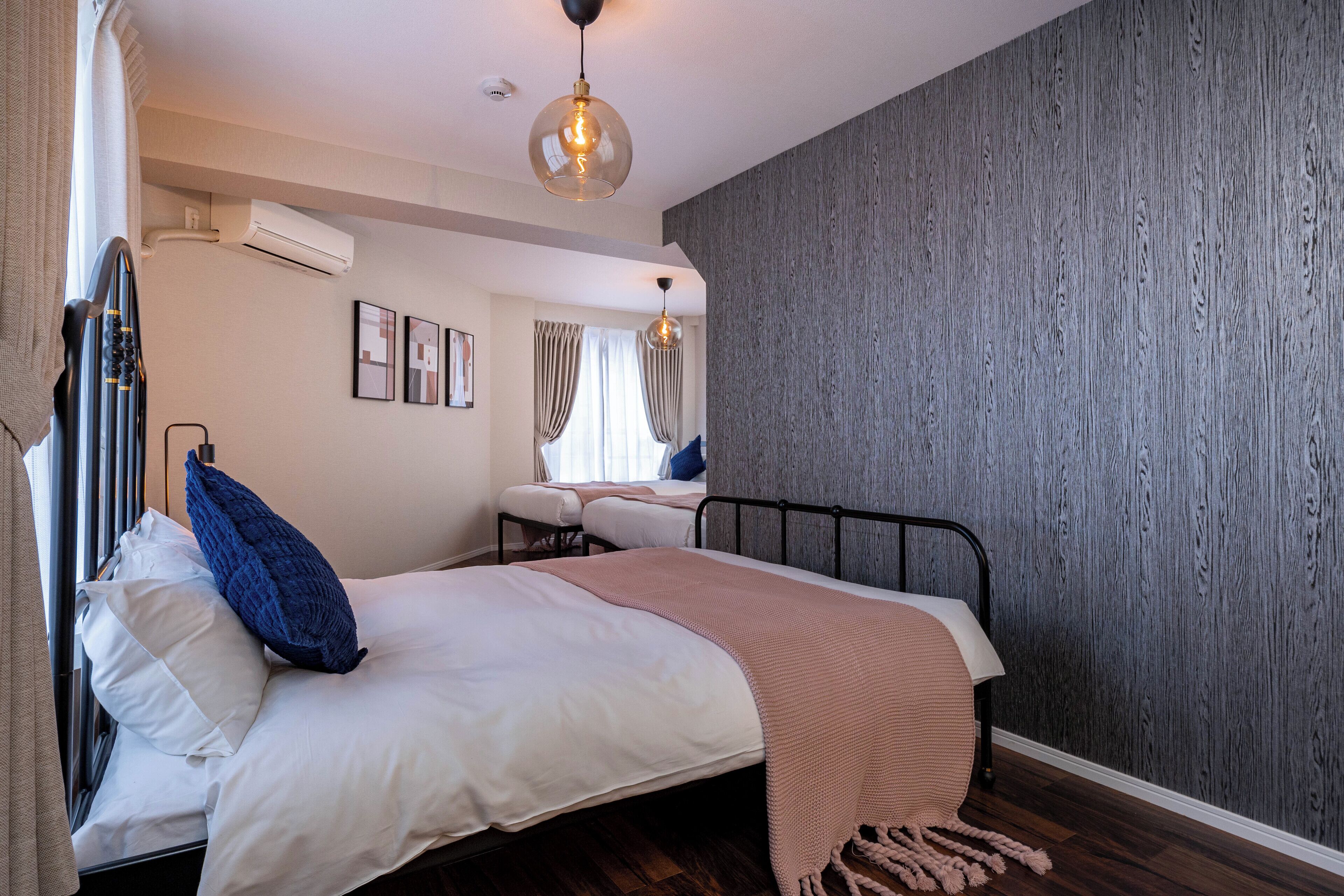 A bedroom with a bed, a window with curtains, a wall-mounted air conditioner, and a ceiling light fixture.
