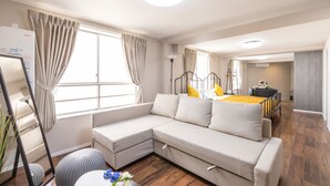 A modern living room with a sectional sofa, a dining area, and a large window with curtains. - Arita Nipponbashi-nishi (Osaka)