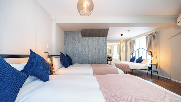 A hotel room with three beds, a wooden accent wall, and a large mirror reflecting the room. - Arita Nipponbashi-nishi (Osaka)