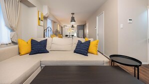 A modern living room with a sofa, a coffee table, and a dining area in the background. - Arita Nipponbashi-nishi (Osaka)