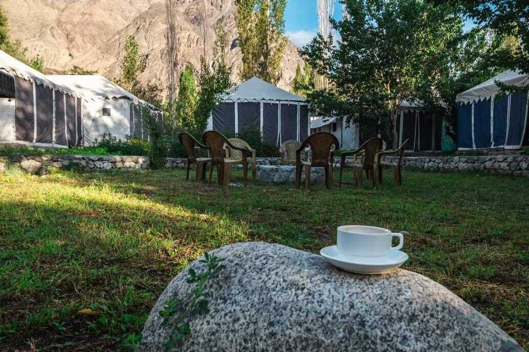 Yurts with outdoor seating, a cup on a rock, and a mountainous backdrop.