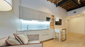 A modern kitchen with white cabinets, a built-in oven, and a dining area with a white table and chairs. - Monti Panisperna Suites (Rome)