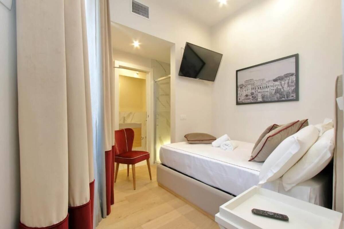 A hotel room with a bed, a chair, a TV mounted on the wall, and a remote control on a bedside table.