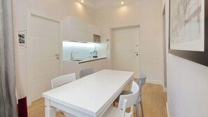 A modern, minimalist room with a white table and chairs, a kitchen area with a built-in oven, and a wooden ceiling. - Monti Panisperna Suites (Rome)