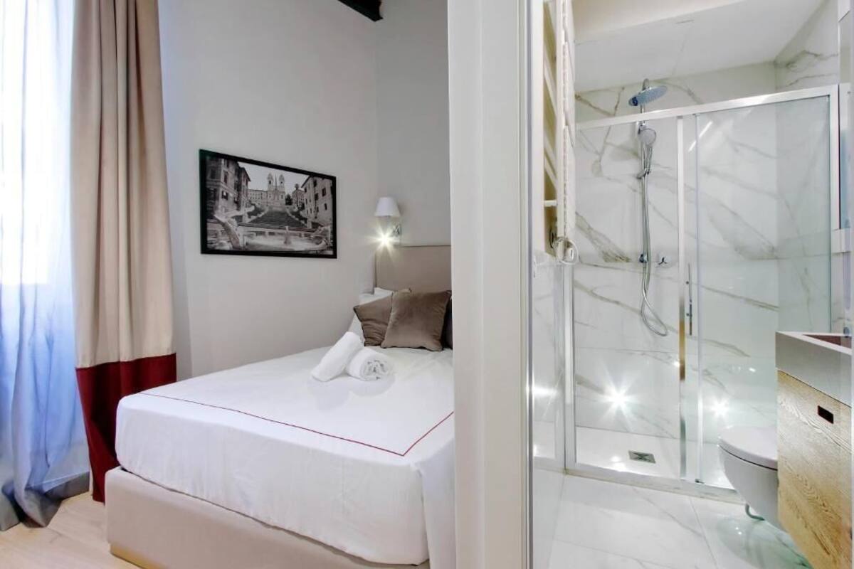 A hotel room with a bed, a framed picture on the wall, a bedside lamp, and a glass-enclosed shower area.