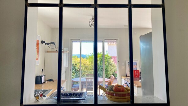 Una habitación con un ventanal grande, una zona de comedor con mesa y sillas, y una cocina con pileta y mostrador.