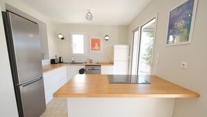 Una cocina moderna con un refrigerador de acero inoxidable, una encimera de madera, lavavajillas y un amplio ventanal que proporciona luz natural.