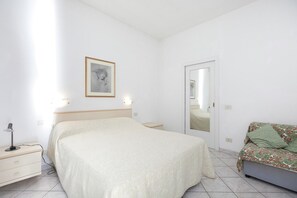 A bedroom with a bed, bedside table, lamp, and a sofa.