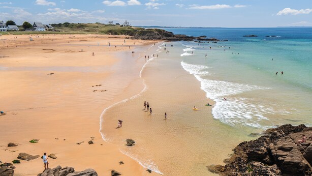 Une plage avec un ciel dégagé, des rivages sablonneux et des affleurements rocheux.