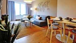 Una sala de estar moderna con un sofá, una mesa de centro y una mesa de comedor. Hay un ventanal con cortinas, una lámpara y una obra de arte en la pared.