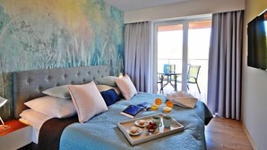 Un dormitorio con una cama grande, una mesita de noche con lámpara, una bandeja con alimentos para el desayuno y vistas al exterior a través de una puerta corrediza.