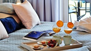Una cama bien hecha con almohadas, una bandeja con artículos de desayuno como magdalenas, fresas y zumo de naranja, y un libro sobre la cama.