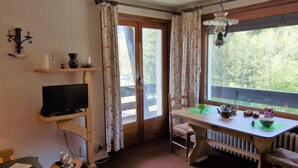 A cozy room with a bed, a TV on a shelf, a table with a kettle, and a window with curtains. - Alpen Roc by Interhome (Chamonix - Les Praz)