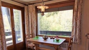 A dining area with a wooden table, two chairs, a radiator, and a window with curtains. - Alpen Roc by Interhome (Chamonix - Les Praz)