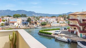 Un pueblo costero con edificios a lo largo de un muelle, barcos amarrados y montañas al fondo.