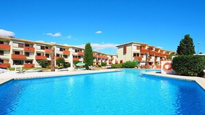 Una piscina rodeada de edificios de varios pisos con balcones, un flotador salvavidas y un cielo azul despejado.