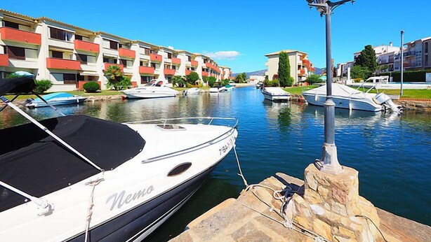 Un puerto deportivo con barcos amarrados, una hilera de edificios de varios pisos con balcones y un farol.