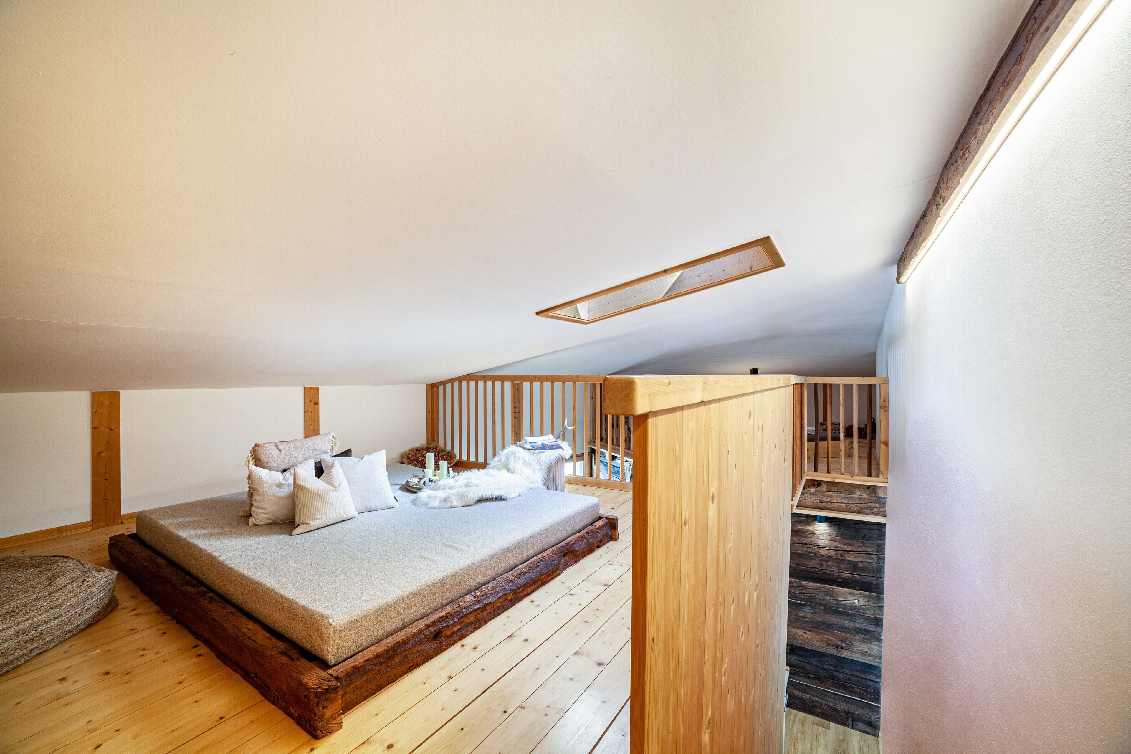 Ein Schlafzimmer mit Holzboden, einem Bett mit Kissen, einem Holz-Kopfteil und einer geneigten Decke mit Leuchte.