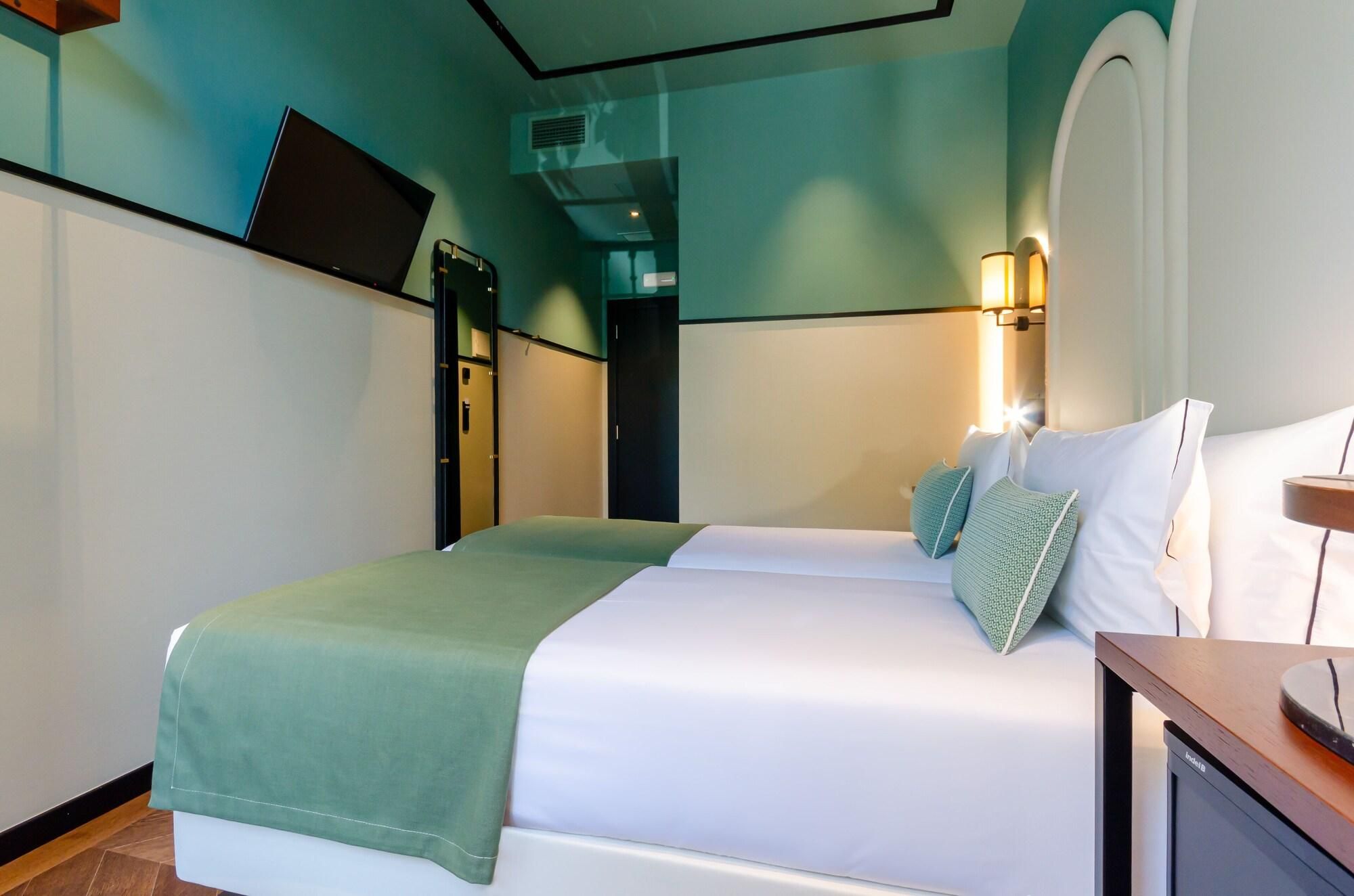 A hotel room with a bed, bedside table, lamp, and a television on a stand.