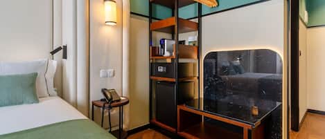 A hotel room with a bed, a desk with a phone, a minibar, and a mirror.