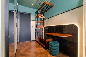 Een modern interieur met een visgraatparketvloer, een houten bankje, een smaragdgroen poef en een zwarte marmeren wand met een inbouwplank.