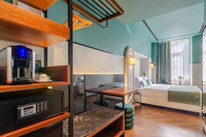 A hotel room with a bed, bedside table, coffee machine, and a desk with a computer.