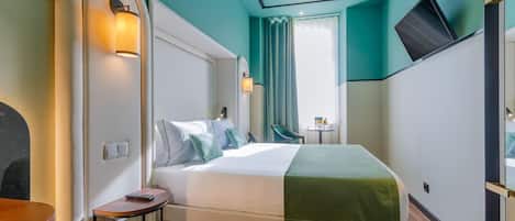 A modern hotel room with a large bed, bedside tables, a chair, and a TV on the wall.