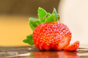 Een aardbei met een groen blaadje op een spiegelend oppervlak.