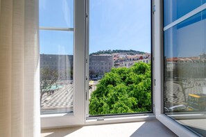 Une chambre d’hôtel dotée d’une grande fenêtre donnant sur un paysage urbain historique, avec ses bâtiments et sa fontaine.