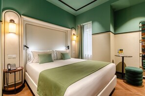 Une chambre d’hôtel avec un grand lit, un téléphone sur la table de chevet, une petite table et un pouf vert.