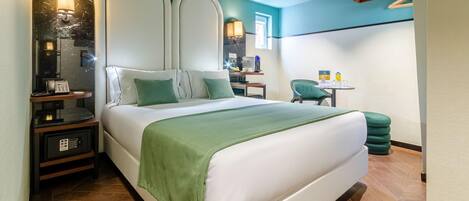 Una habitación de hotel moderna con una cama grande, un escritorio con silla, una mesita pequeña y un reposapiés verde.