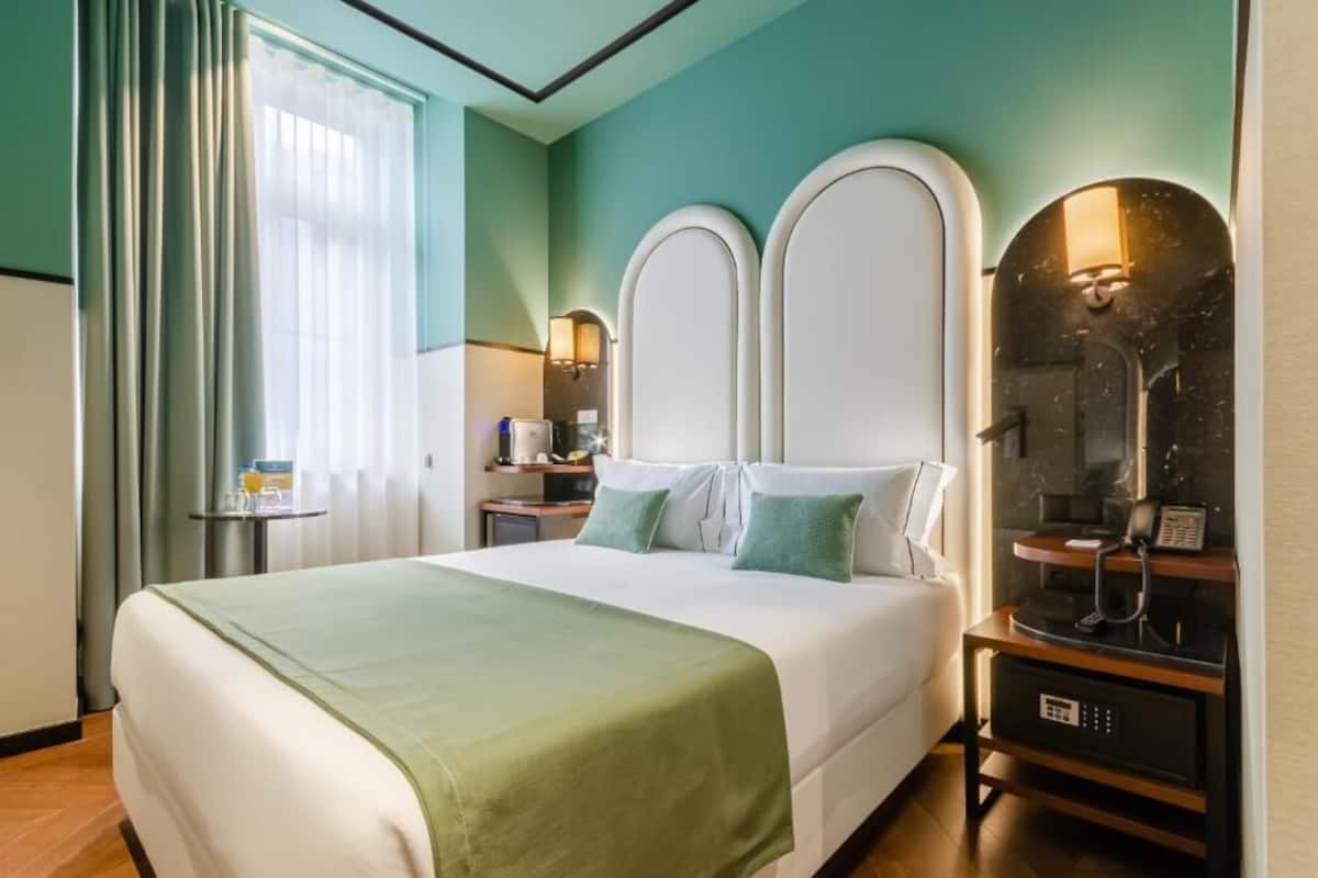 A hotel room with a large bed, a bedside table with a lamp, a mirror, and a telephone.