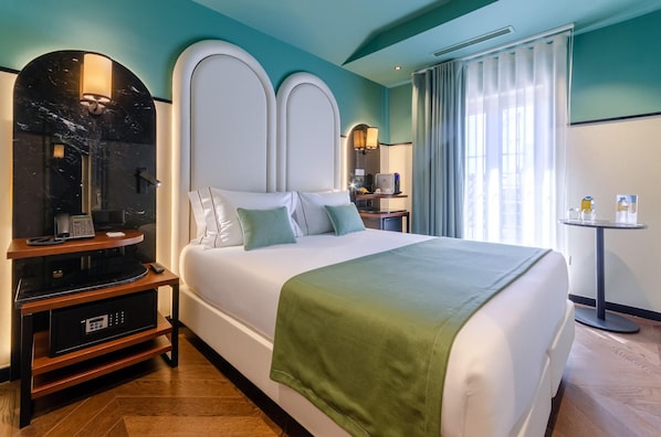A hotel room with a large bed, a desk with a phone and a computer, a mirror, and a window with curtains.