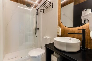 Un baño moderno con ducha envuelta en vidrio, inodoro blanco y lavamanos grande sobre encimera negra.
