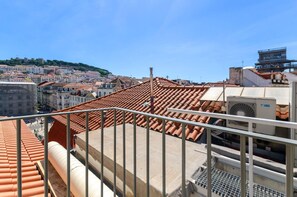 Une terrasse sur le toit, avec des carreaux de terre cuite, une rambarde en métal et un appareil de climatisation.
