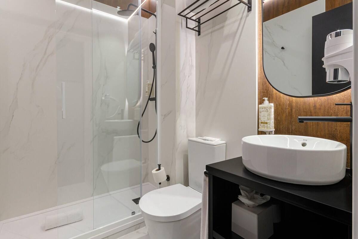 A modern bathroom with a glass-enclosed shower, a white toilet, and a vanity with a large mirror and a sink.