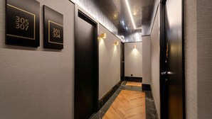 Un couloir moderne avec des portes noires, des plaques numérotées et un plancher en bois.