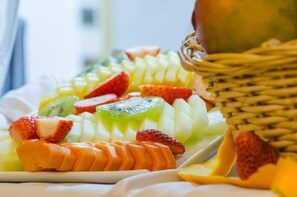 Een fruitschaal met plakjes aardbeien, kiwi, mango en ananas op een wit bord.