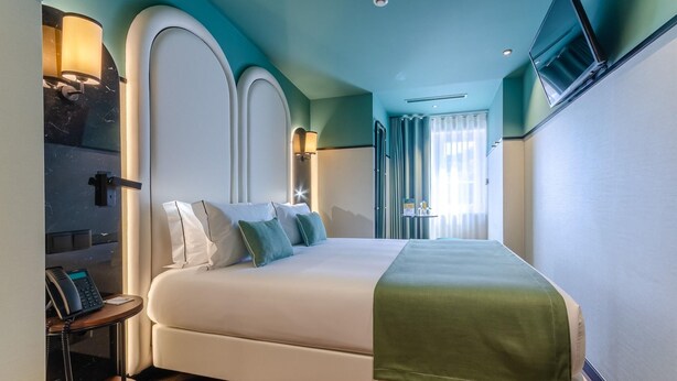 Une chambre d’hôtel équipée d’un lit, d’un bureau avec un téléphone et d’un téléviseur fixé au mur.