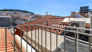 Une terrasse sur le toit, avec des carreaux de terre cuite, une rambarde en métal et un appareil de climatisation.