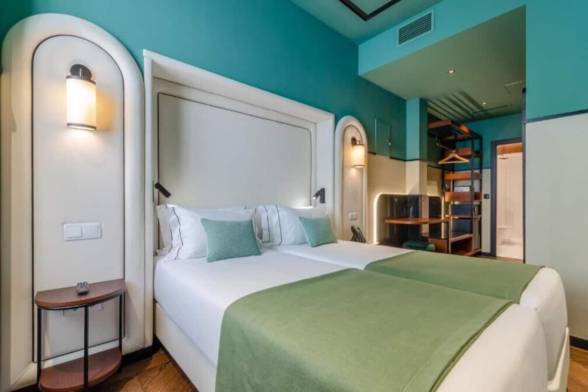 A double bed with a white headboard and green bedding, a bedside table with a lamp, and a wardrobe with a mirror.
