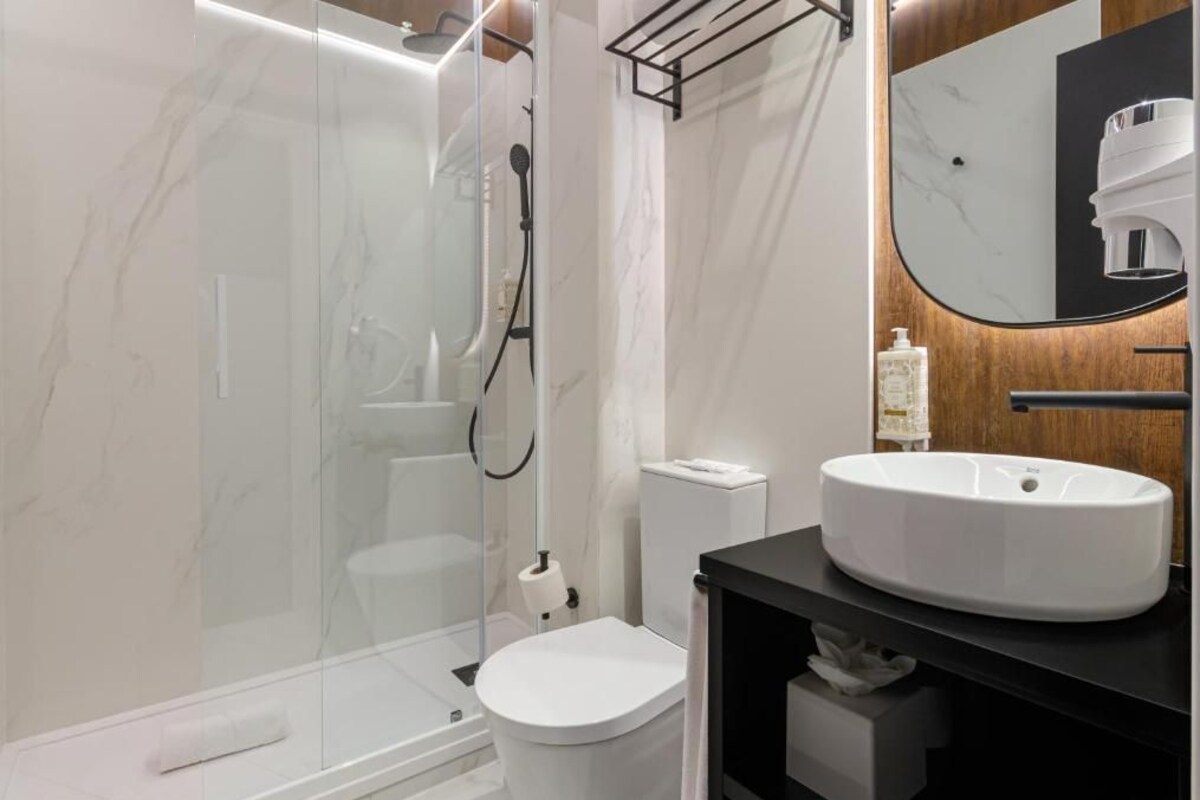 Une salle de bain moderne avec une douche à parois de verre, des toilettes blanches et un meuble-lavabo noir doté d’un grand miroir.