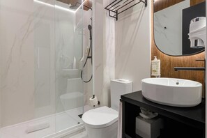A modern bathroom with a glass-enclosed shower, a white toilet, and a black vanity with a large mirror. - Nicola Rossio Hotel (Lisbon)