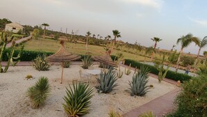 A garden with cacti, palm trees, and a thatched-roof table and chairs. - SUMAHAN SUITES & SPA (Tameslouht)
